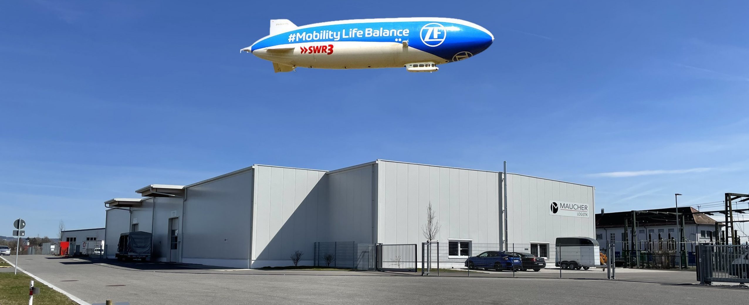 Exterior view of the Maucher logistics hall in Meckenbeuren with the ZF/SWR3 zeppelin "Mobility Life Balance" in the sky above